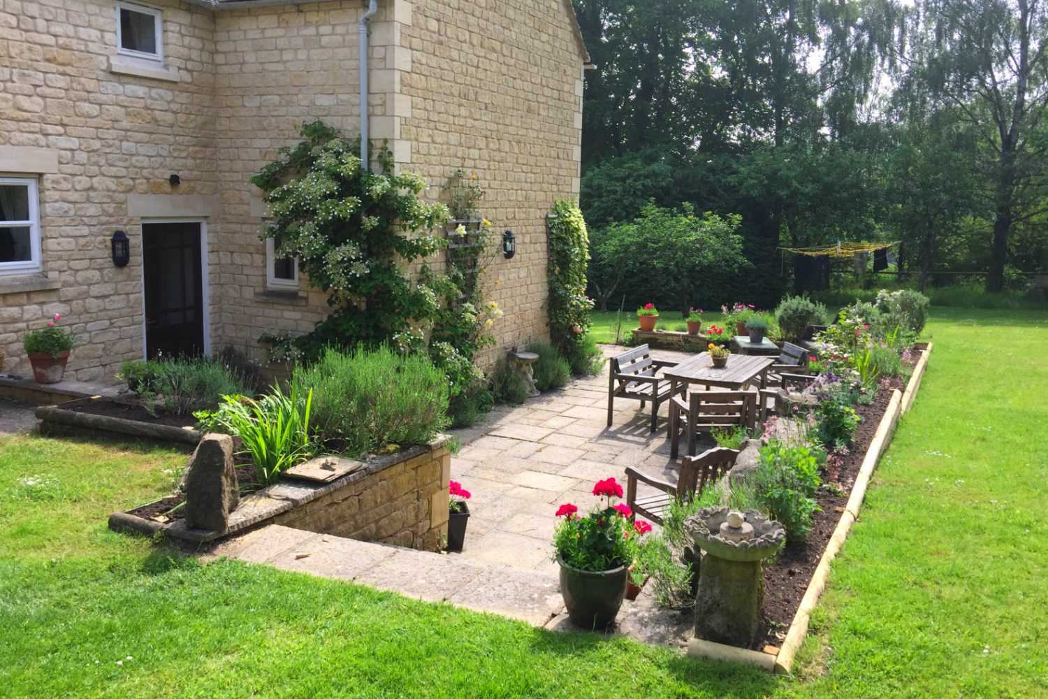 Cotswold stone cottage with paved patio, wooden garden furniture and lawned garden at Whiteshoots House